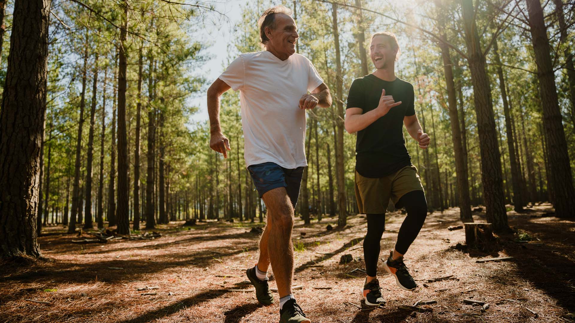 Two men running through woodland on a sunny day