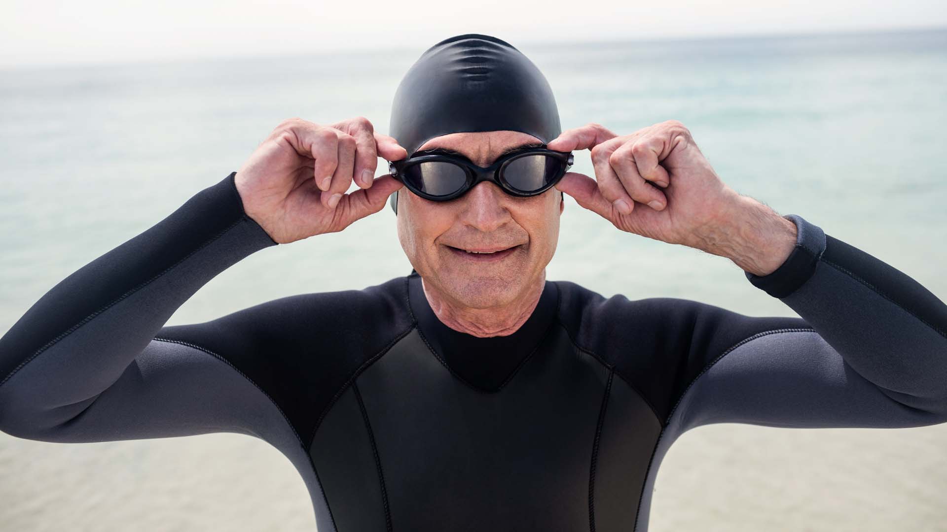A man in googles, a swim cap and wetsuit preparing for an outdoor swim