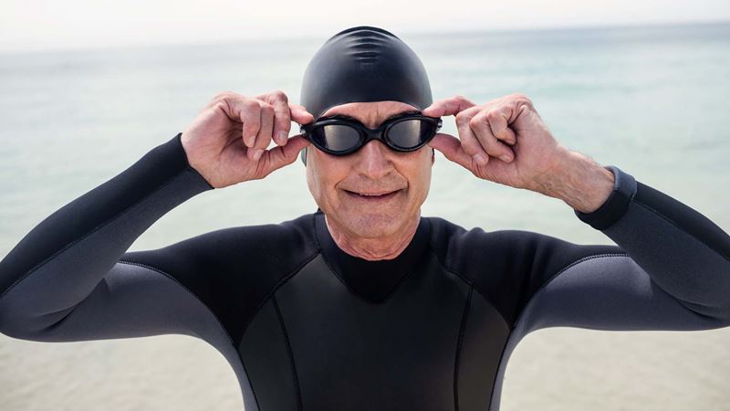 A man in googles, a swim cap and wetsuit preparing for an outdoor swim