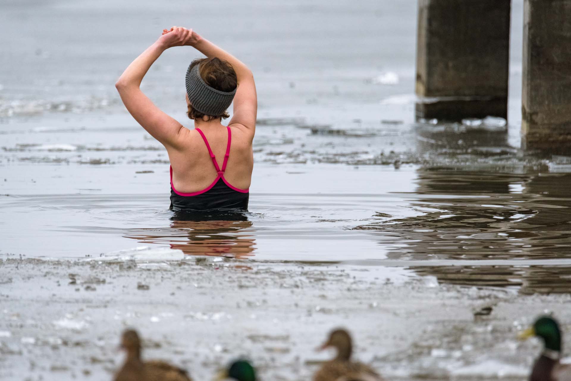 A woman stretching her arms above her head while wild swimming with ducks