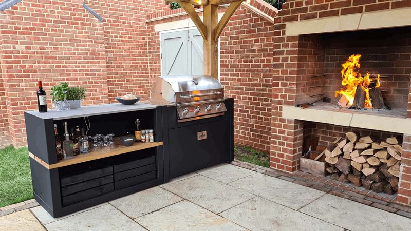 A modern outdoor kitchen unit with BBQ next to a wood burning fire