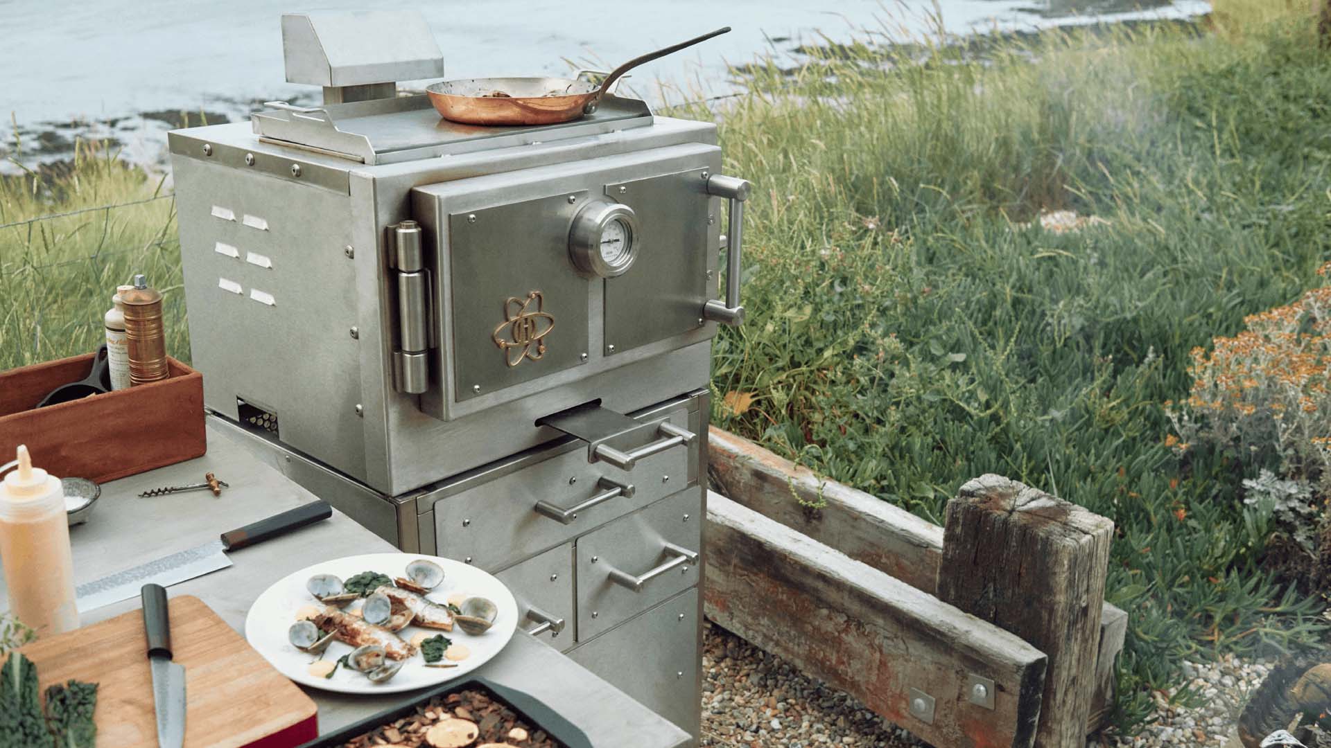 grey, metal dual-fuel barbecue in an outdoor decking area overlooking water
