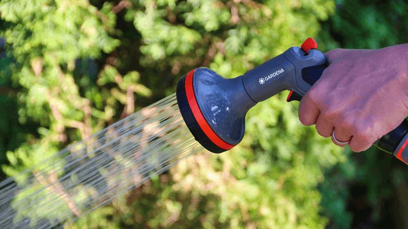 Close-up of a hand holding a hose pipe with sprinkler attachment in a sunny garden.