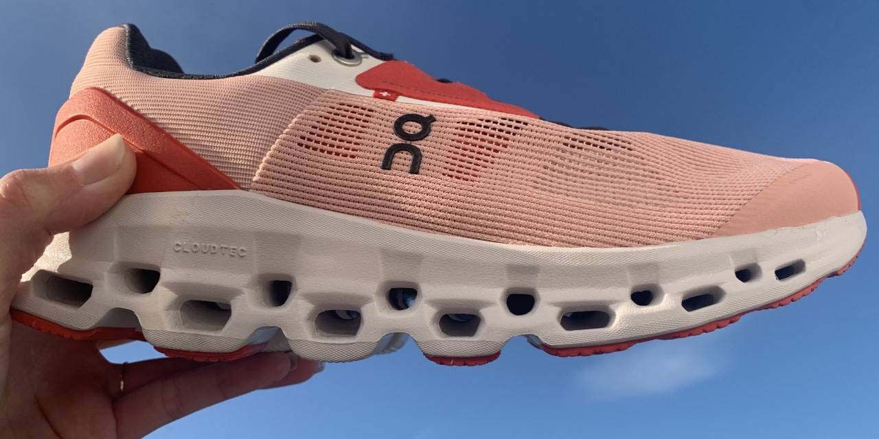 A pink running shoe held up with a blue sky in the background