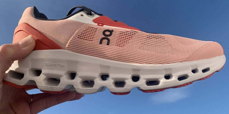 A pink running shoe held up with a blue sky in the background