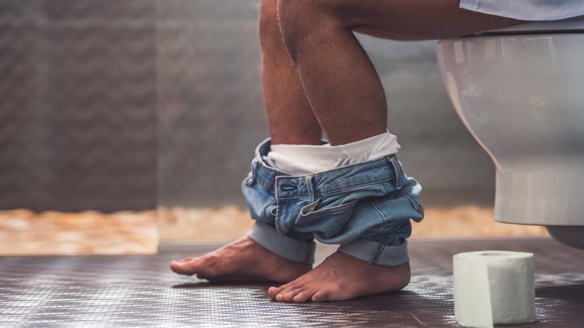 someone's legs with trousers round their ankles sitting on the toilet