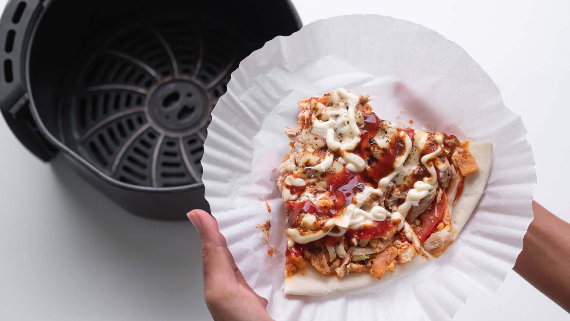 A person pulling pizza into an air fryer