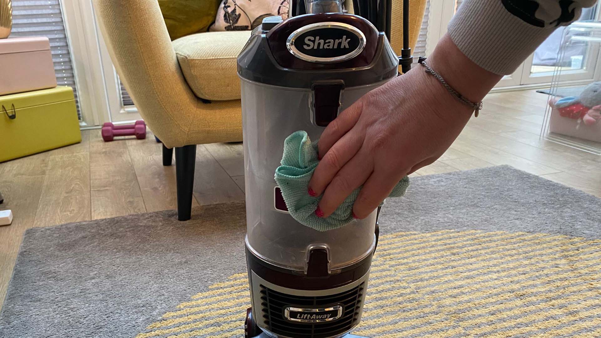 A person cleaning the outside of their vacuum with a cloth