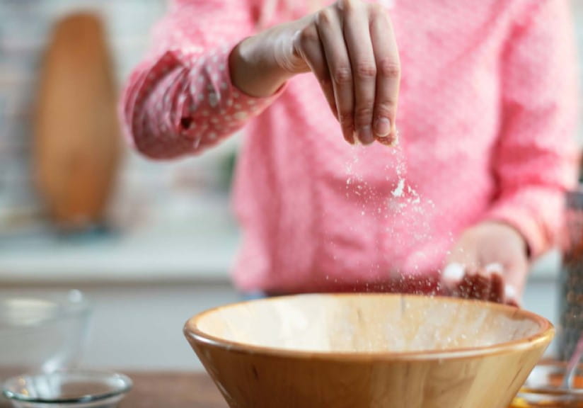 A woman in a pink jumper adding salt into a mixing bowl