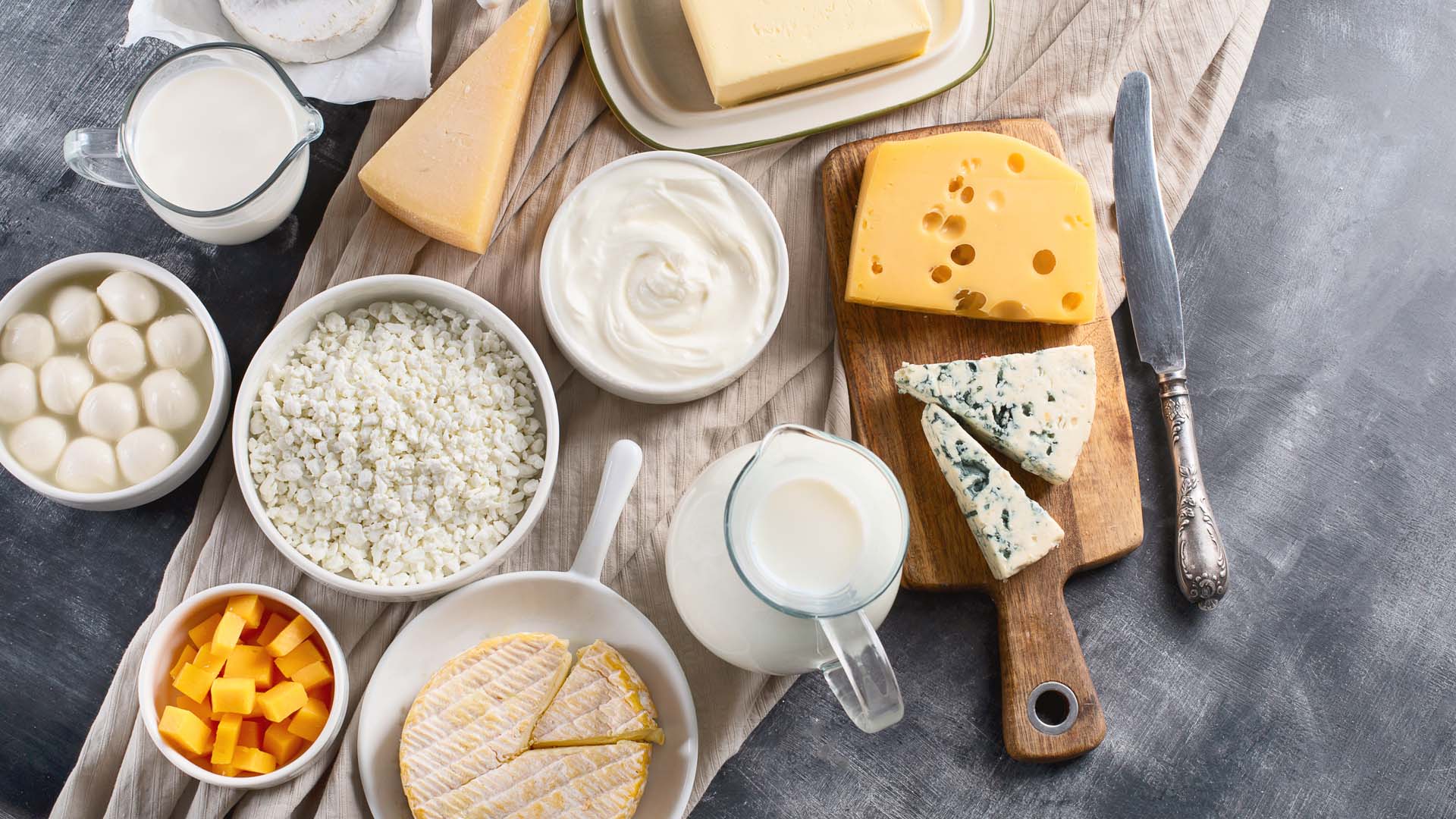 Selection of dairy products including cheeses, yoghurt and milk displayed on a wooden board.