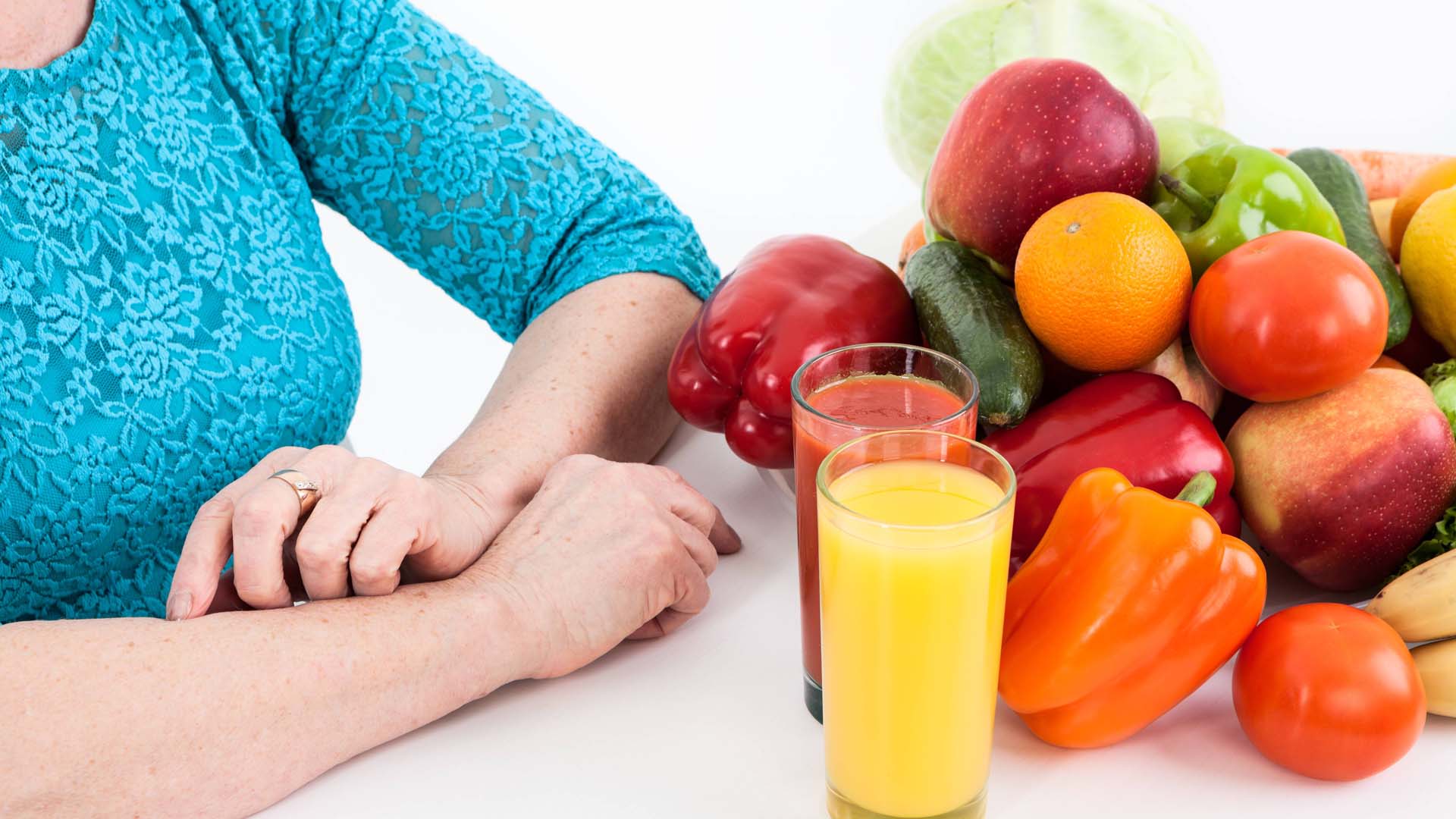 Close-up of a woman sitting in front of a pile of fruit and veg alongside a glass of orange juice.