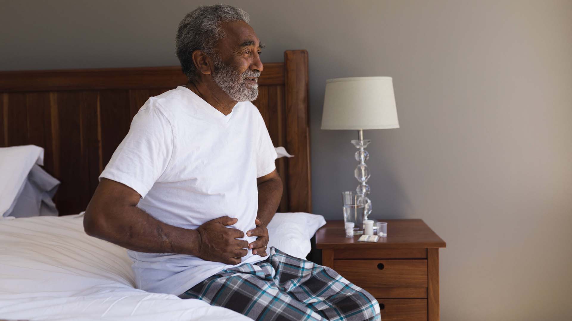 A man sitting in bed clutching his stomach in pain