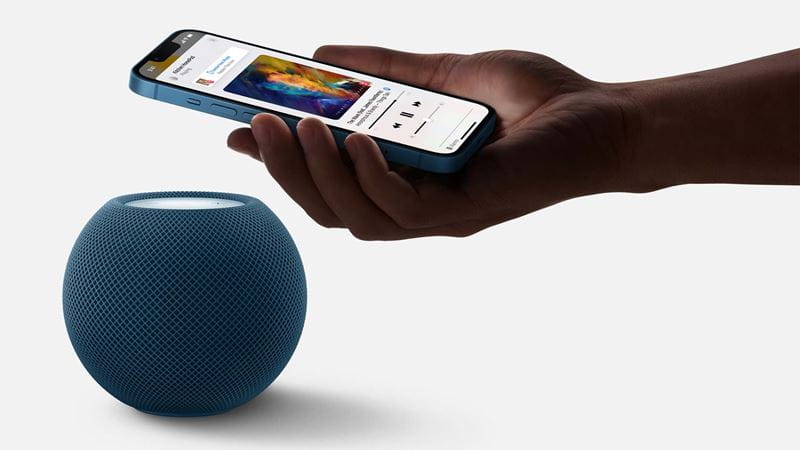 a phone held above a HomePod Mini, as if to use