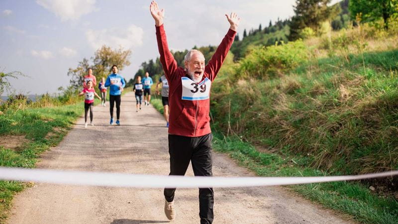 Senior man runner crossing finish line in a race competition in nature.