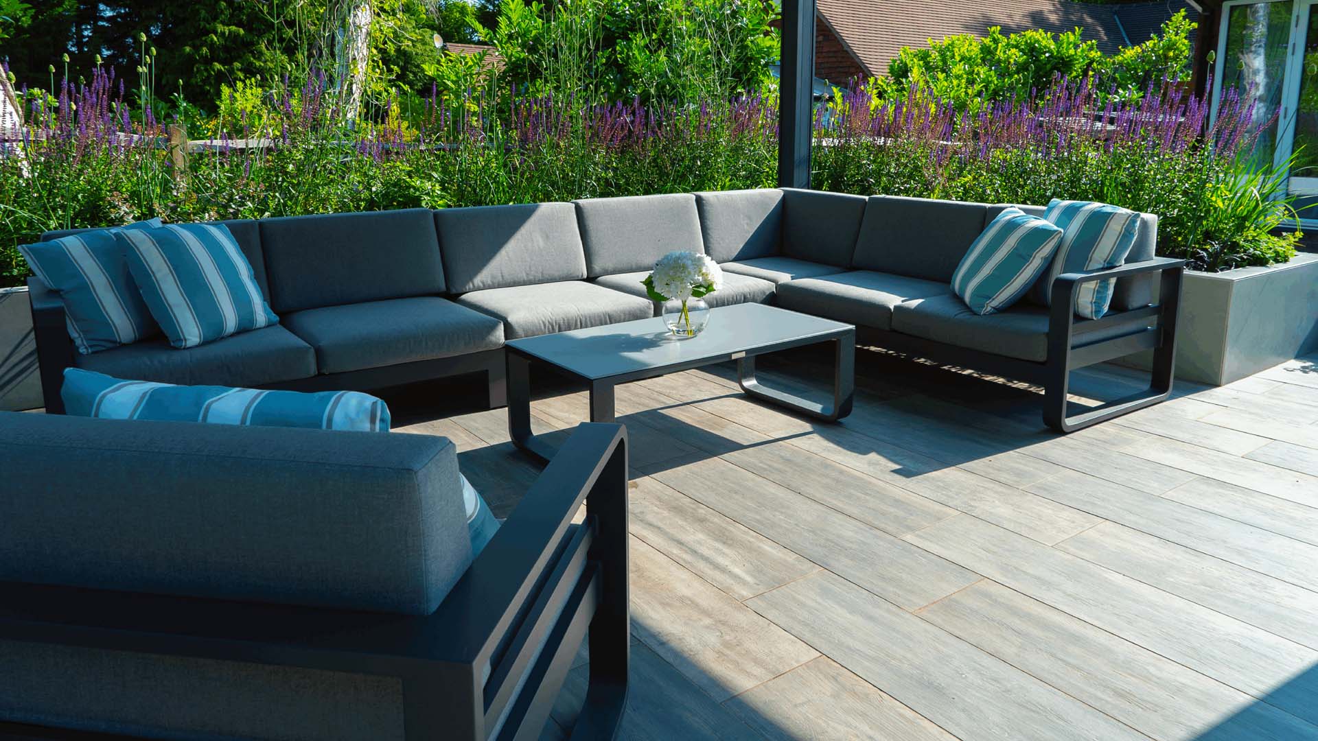 Semi covered garden deck framing an extensive sofa setup with large, raised plant beds