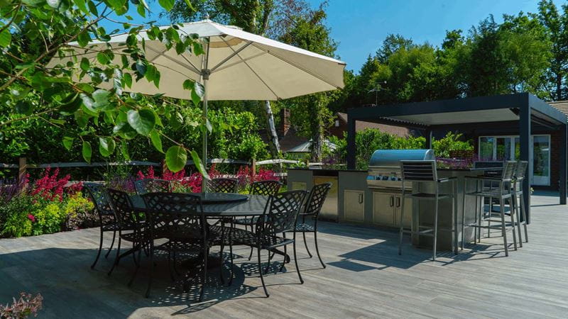 Parasol and metal round table with dining chairs alongside raised bar seating area