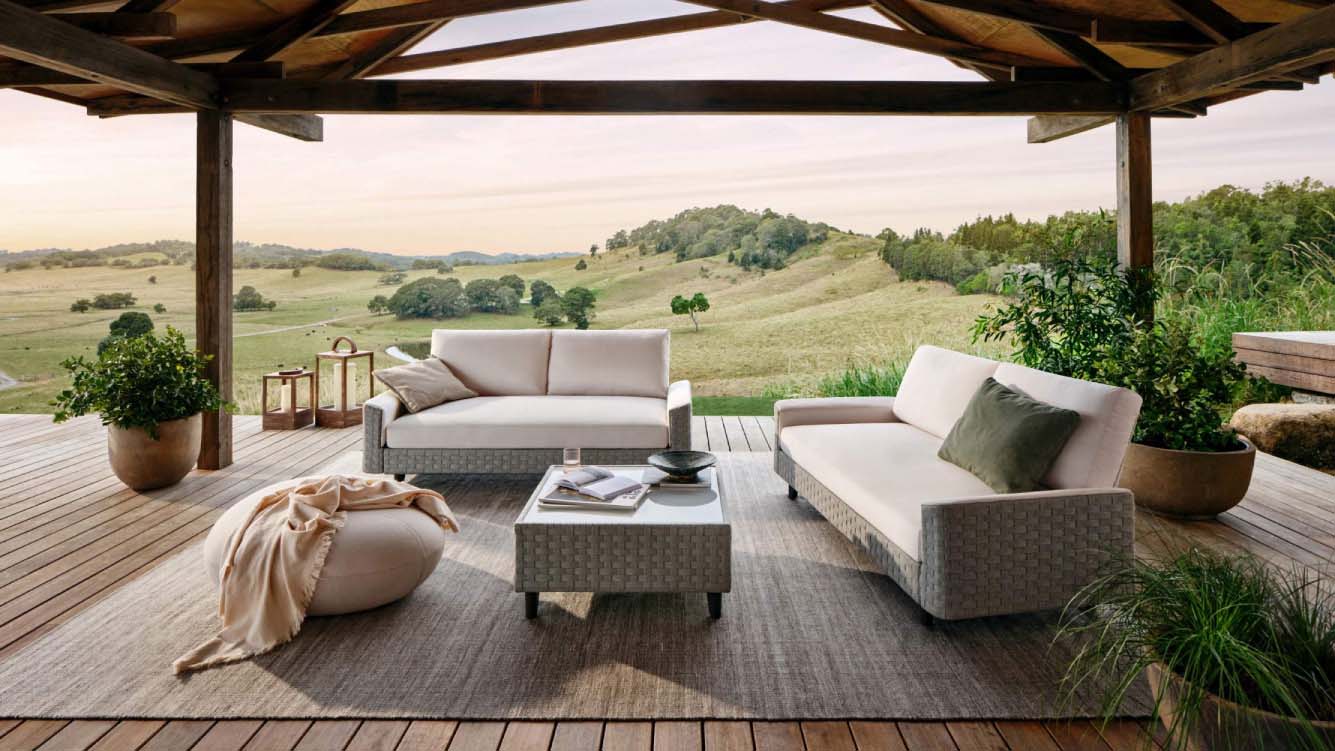 Garden decking covered by a pergola overlooking a hilly countryside vista, with modern outdoor furniture arranged on the decking.