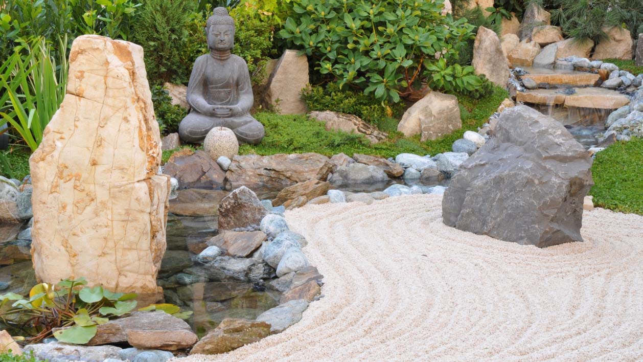 Japanese Zen garden with a sandy pathway, many rocks and a Buda statue in the background 