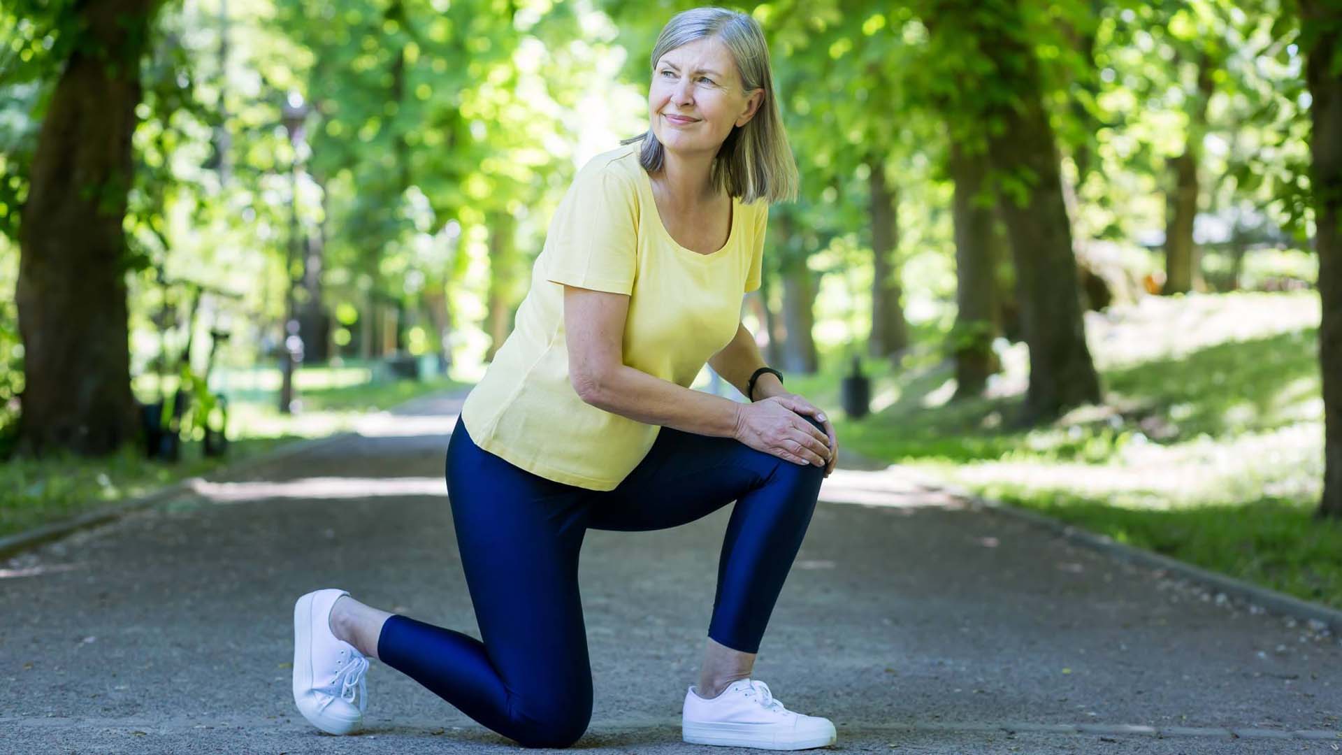 Senior active woman on a jog injured her leg and knee, gray-haired pensioner in a summer park