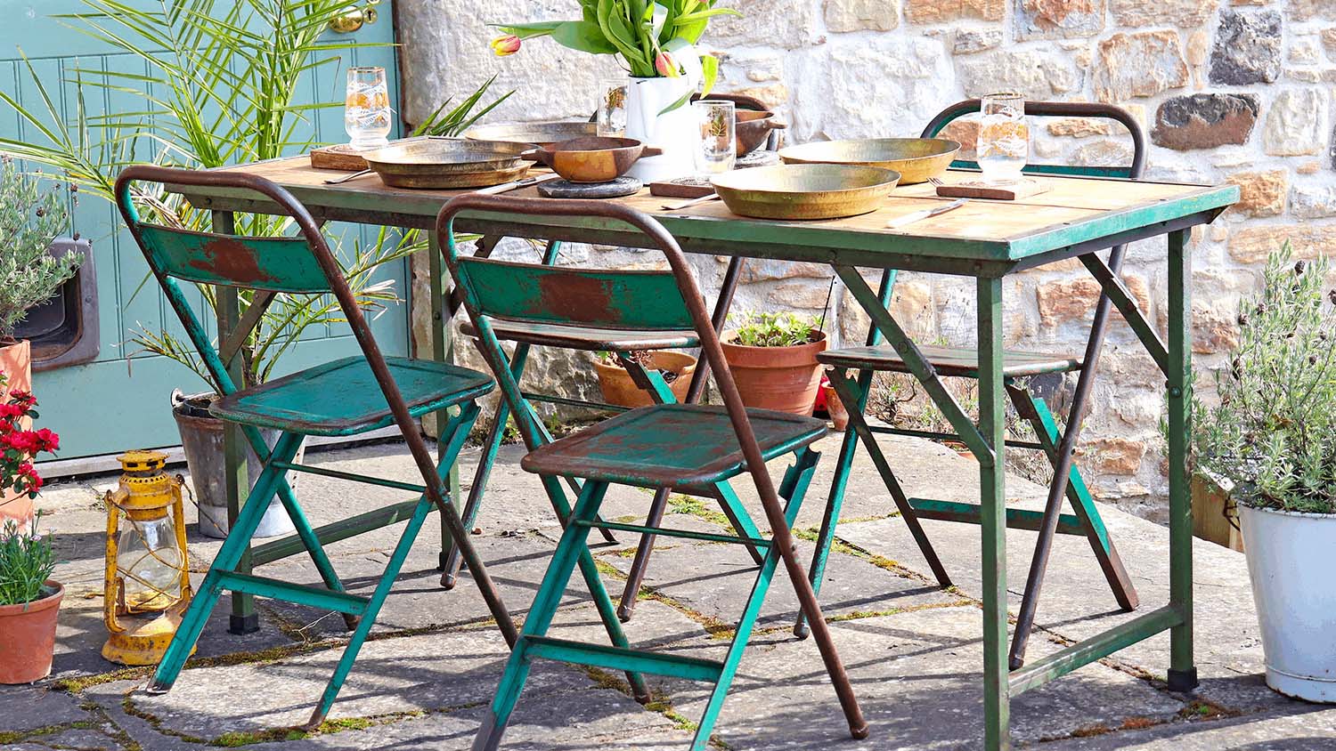 Rustic metal green and oxidized table with 4 chairs in a stone patio surrounded by a few plant pots