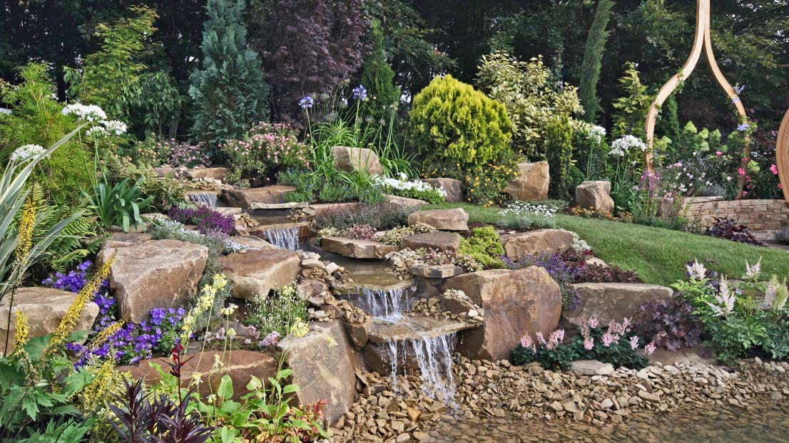A rockery with a waterfall surrounded by flowers and plants.