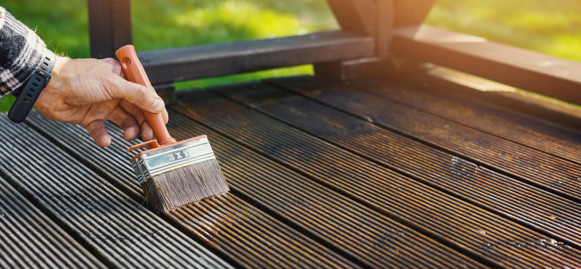 Someone applying wood protection oil on decking boards with paint brush