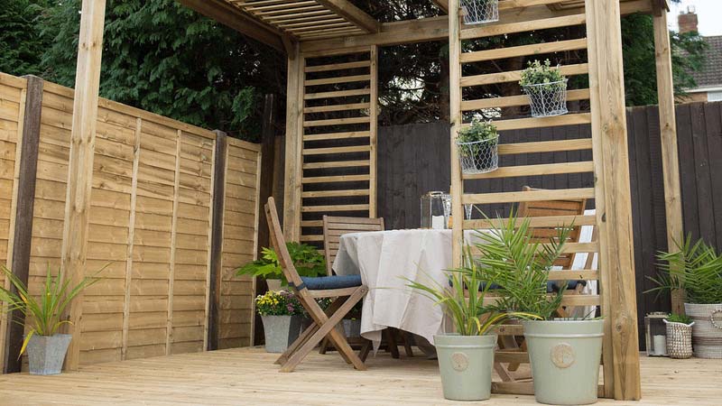 Light wood pergola with plant climbers on a light deck with dinner table and chairs