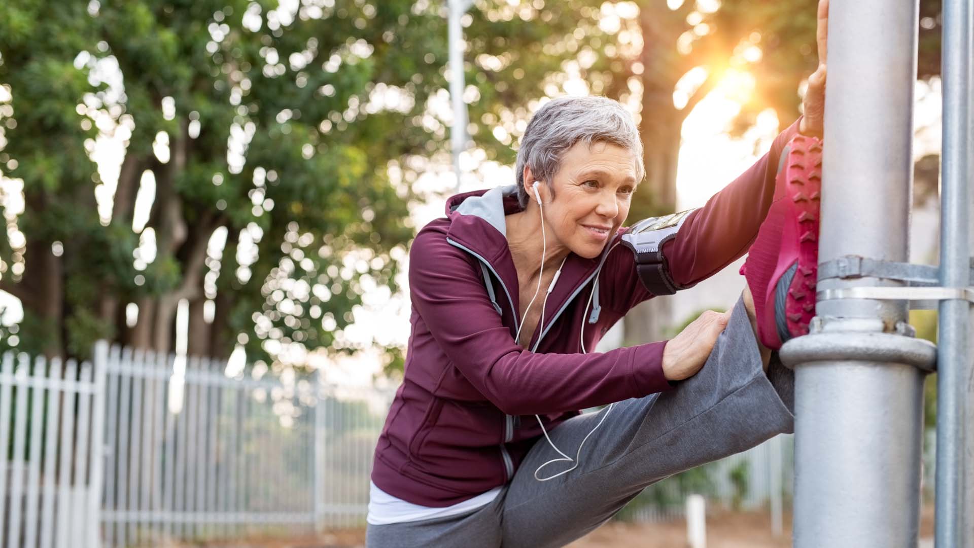 A woman using a street light to stretch her left leg before exercise; warm-up exercises