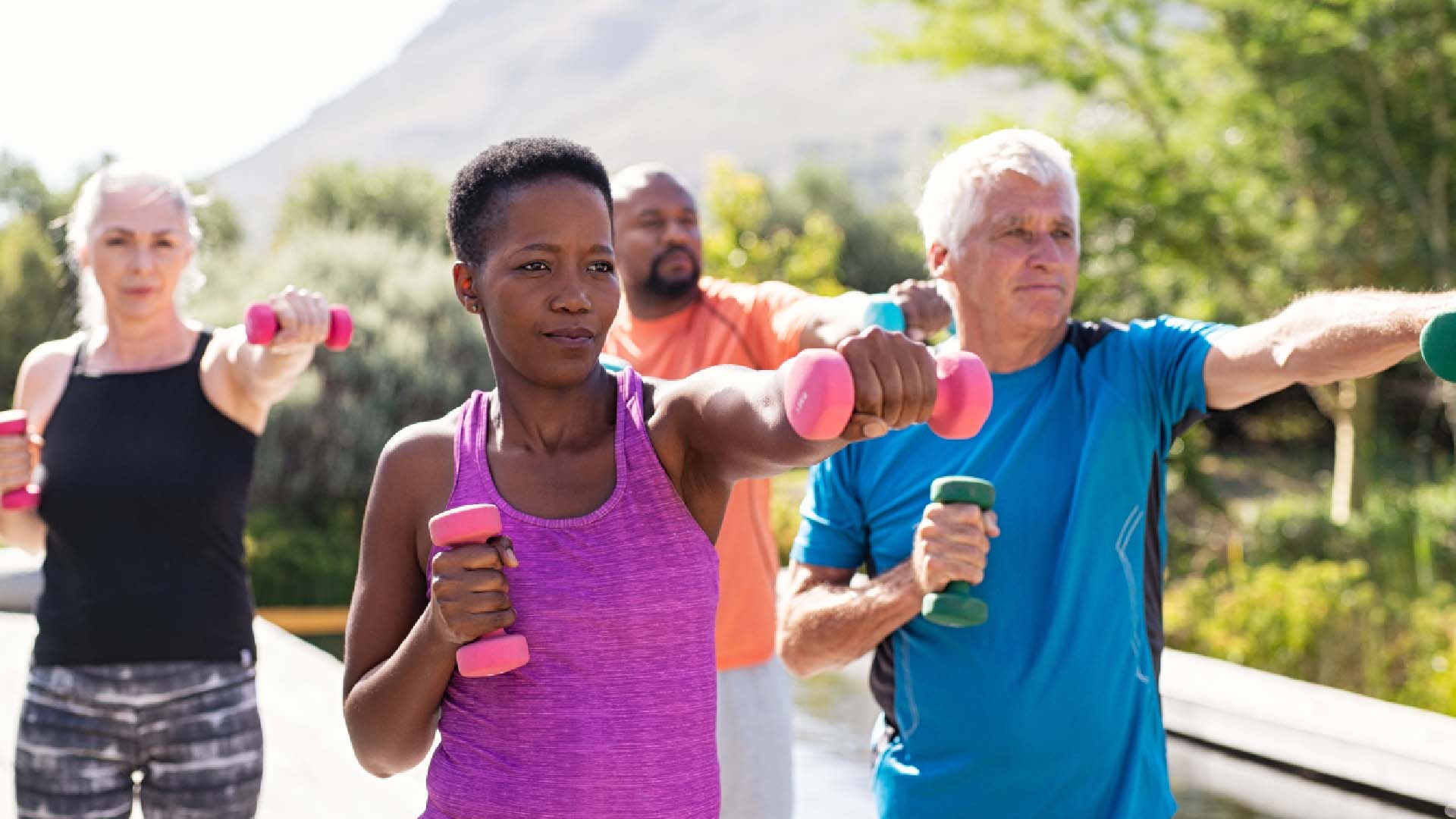 A group of older individuals training with hand weights outdoors on a sunny day