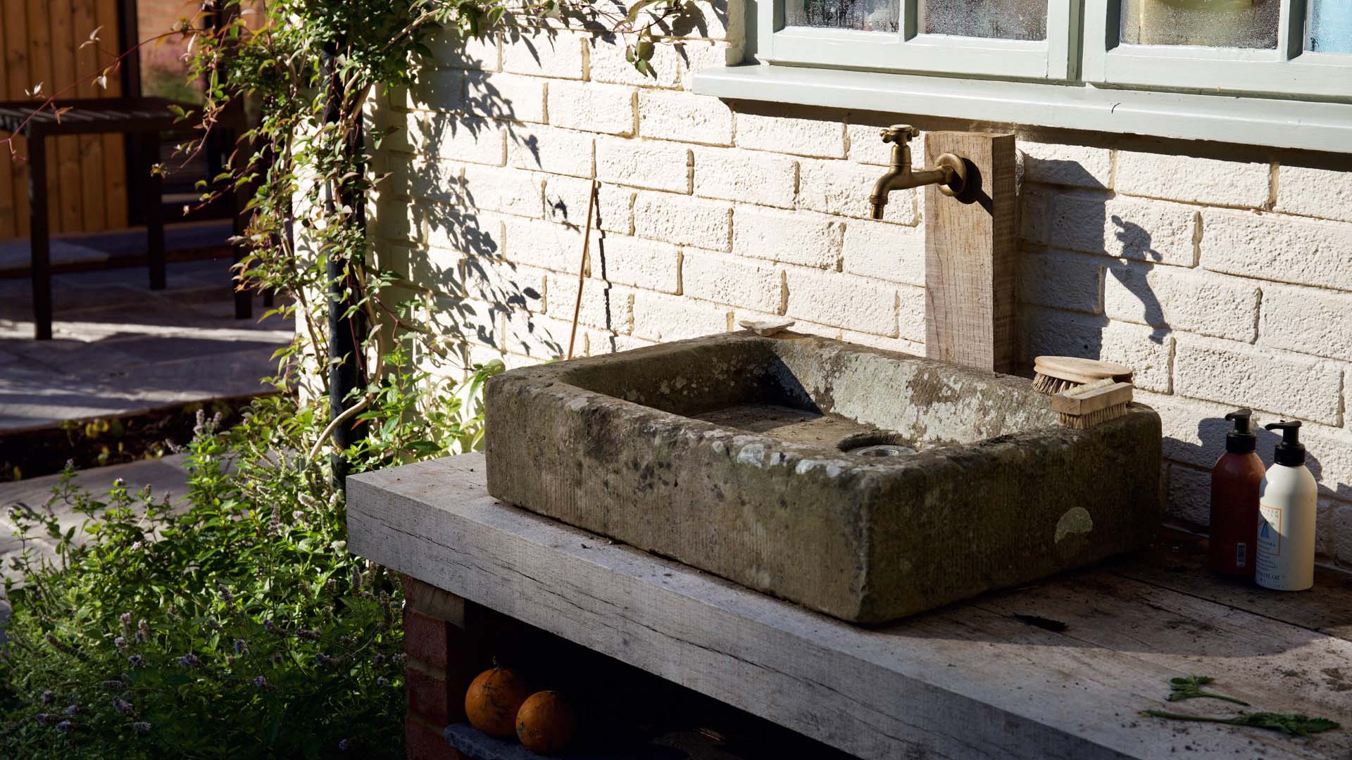 A stone sink against an outdoor wall with a single tap above it