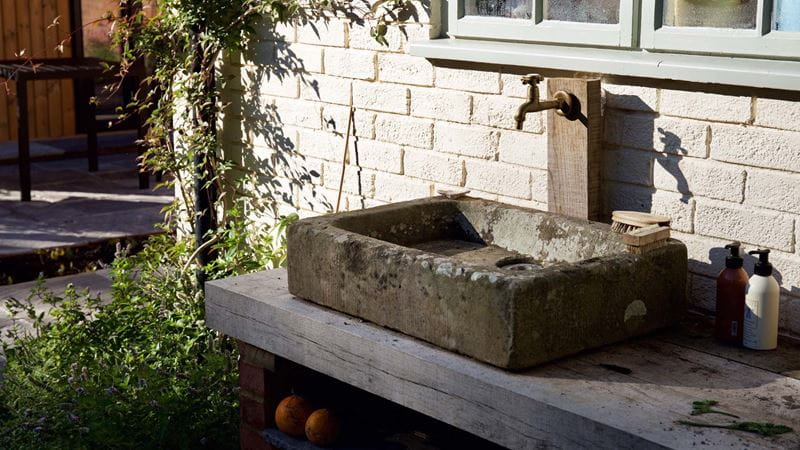 A stone sink against an outdoor wall with a single tap above it