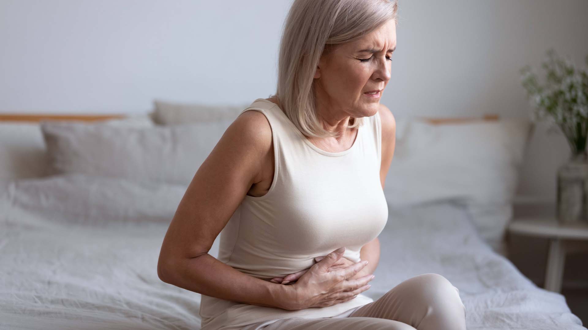 woman sitting on the bed bed holding on to her tummy in pain