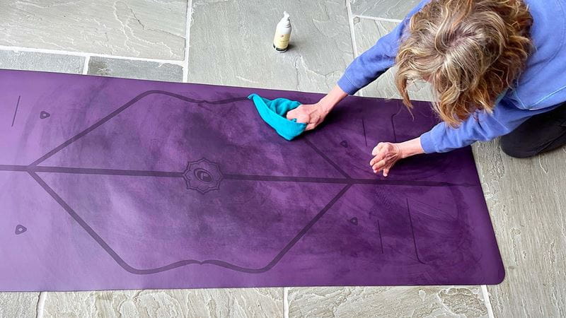 woman scrubbing a purple yoga mat on the floor