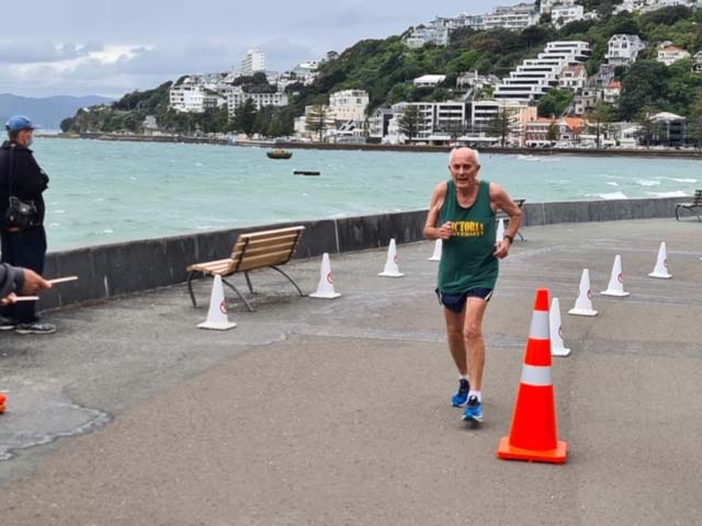 Mature runner Roger Robinson running a 10k race with a seaside view behind him