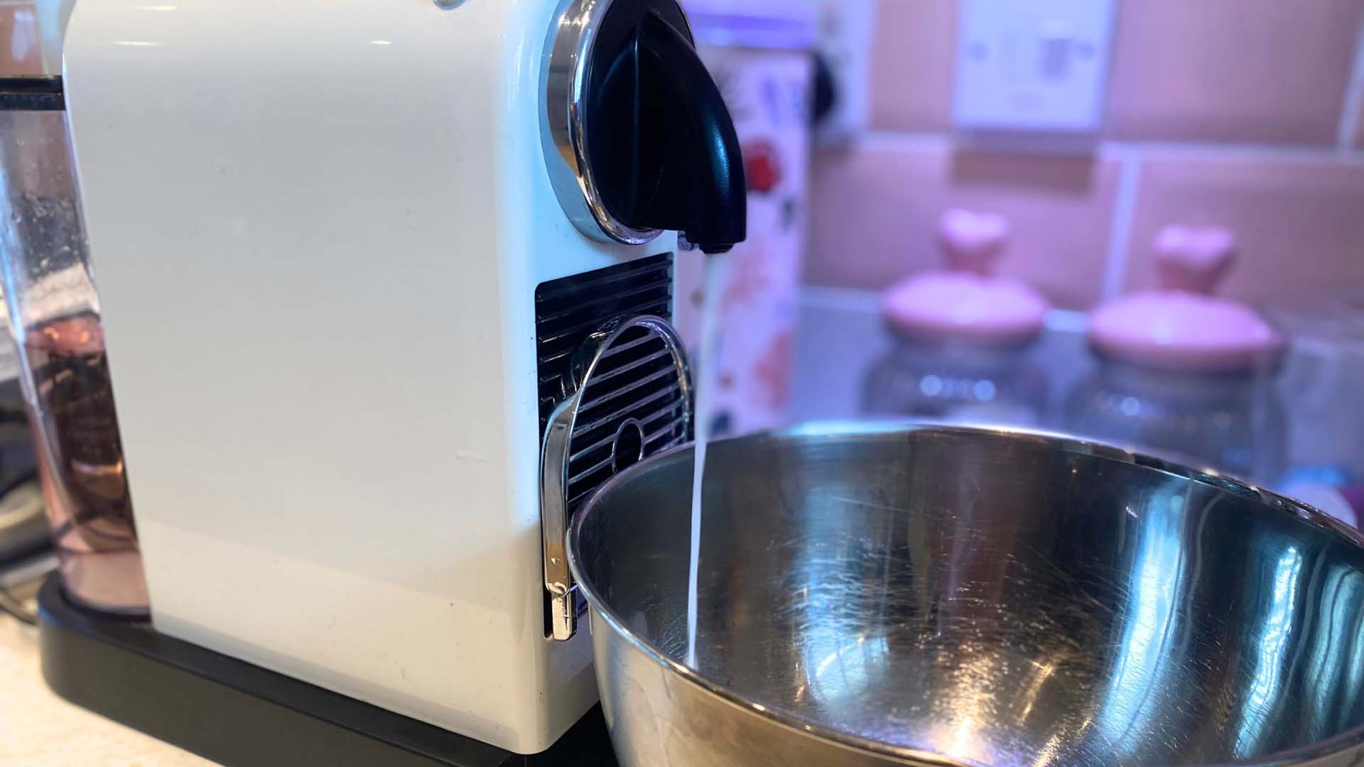 Close-up of a cream coffee pod machine with descaler solution filtering out of the machine into a bowl
