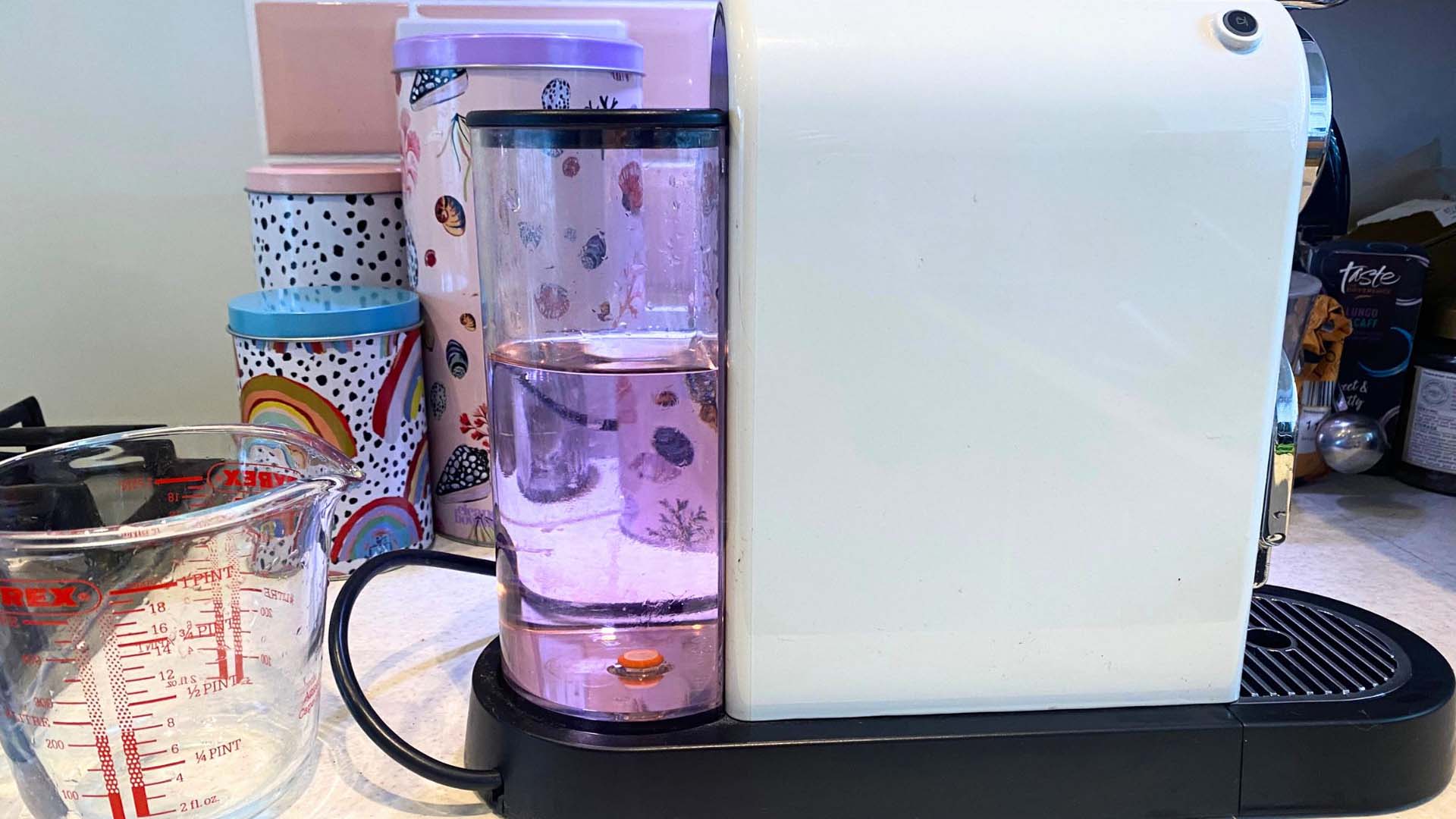 Side view of a cream coffee pod machine and a jug of descaler solution