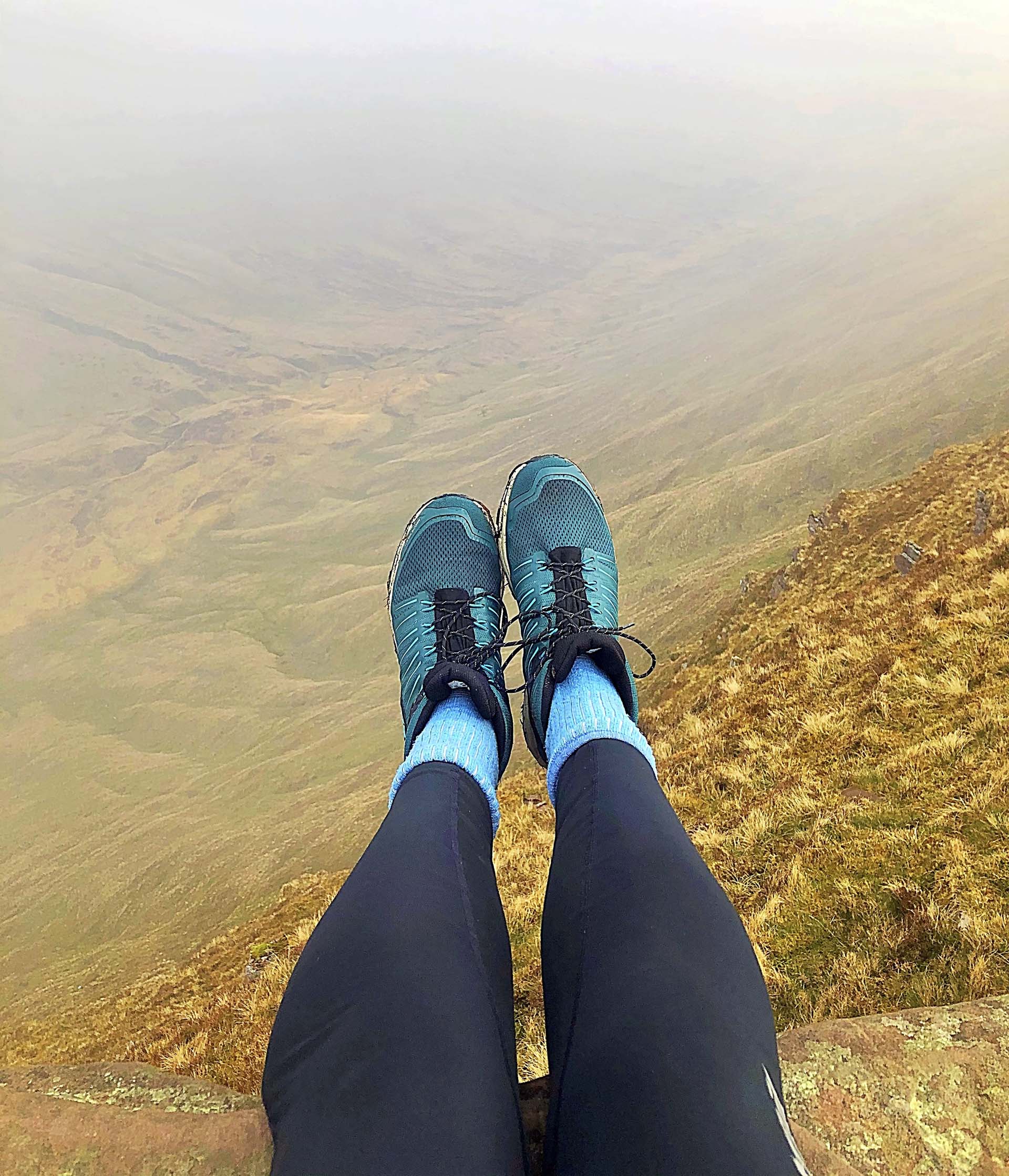 Legs dangle over a ledge on a mountain, wearing properly fitting hiking boots