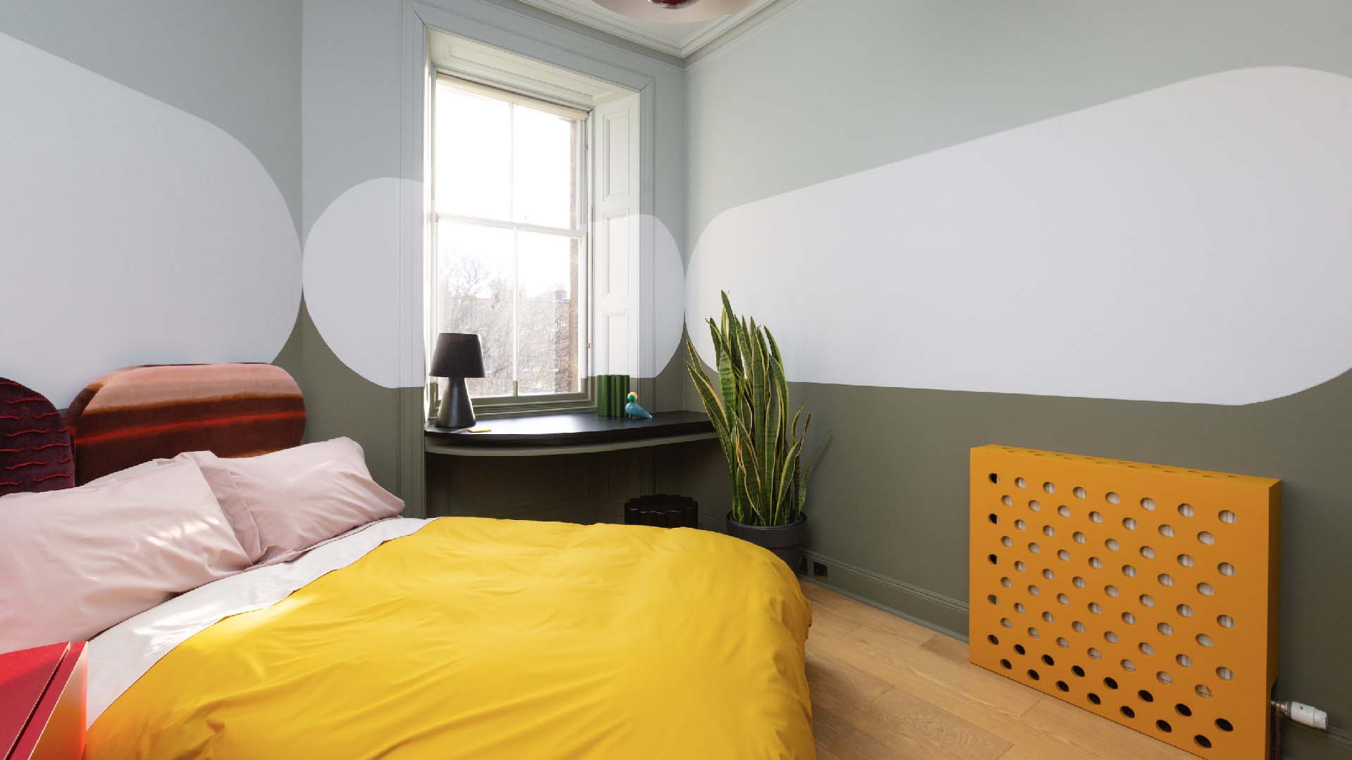 A bedroom with bright soft furnishings and walls painted with soft shapes