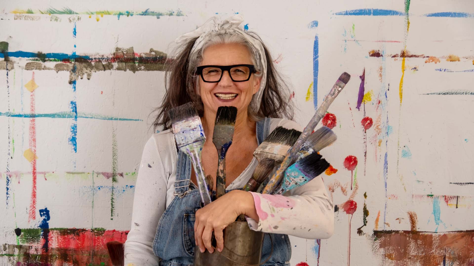 An older woman holding a number of paintbrushes