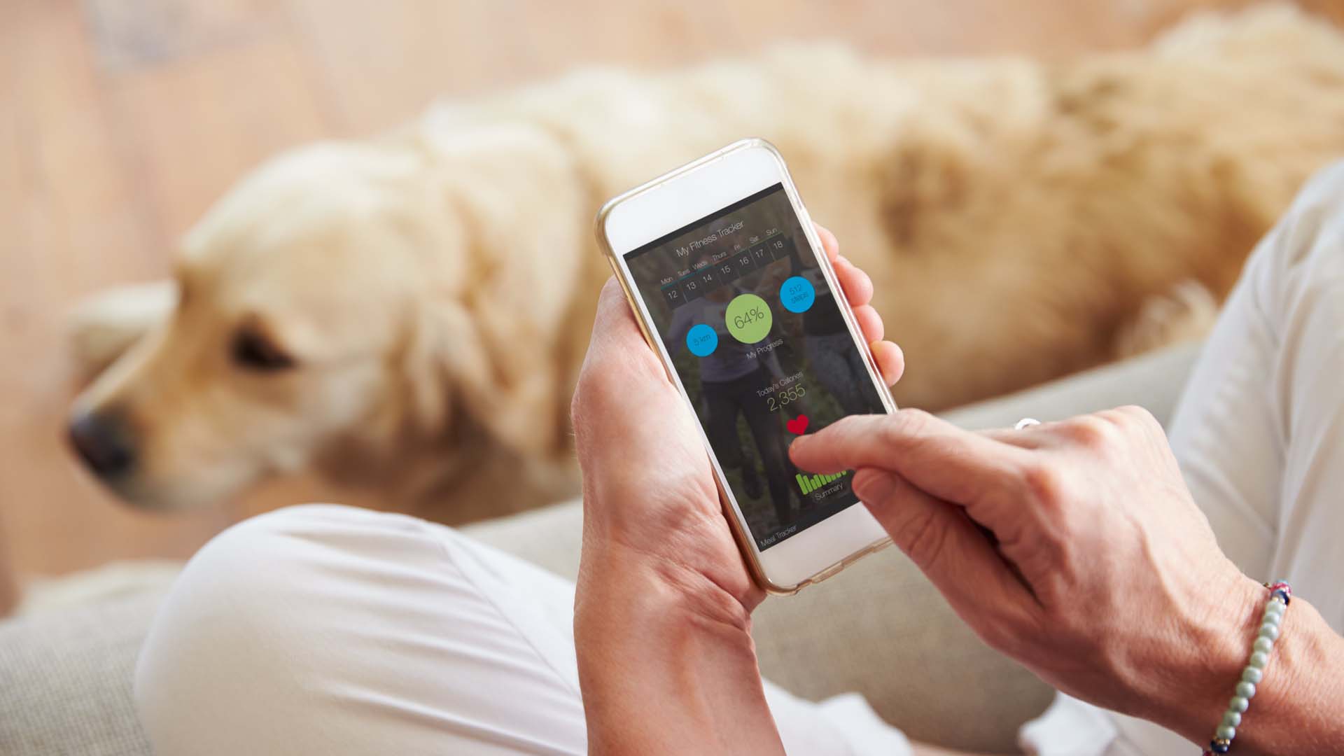 Close-up of a woman using a health app on a phone, with a golden retriever lying by her feet