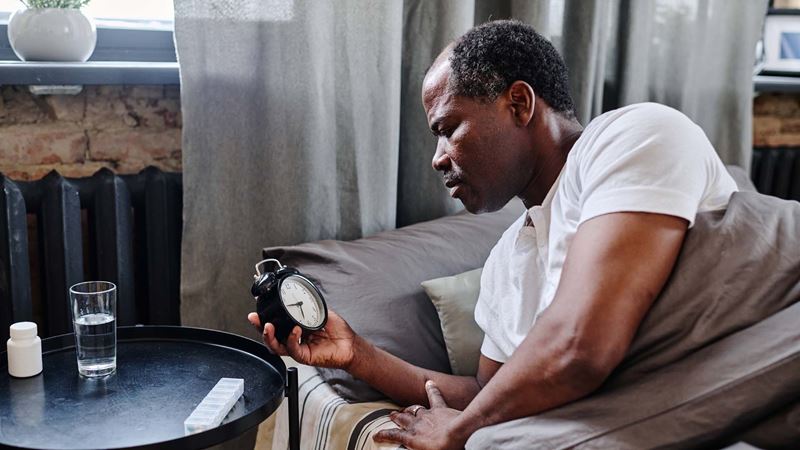Senior man looking at alarm clock deciding how long to nap for
