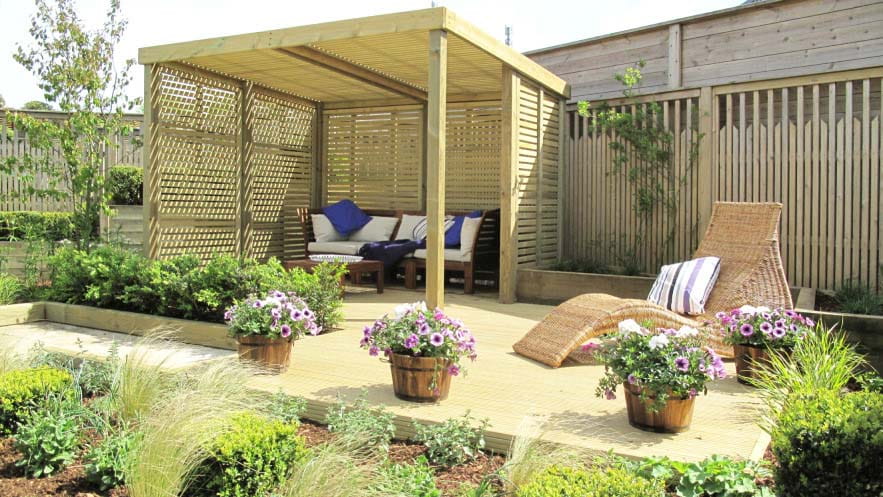 An area of decking in a back garden with a covered terrace at the back