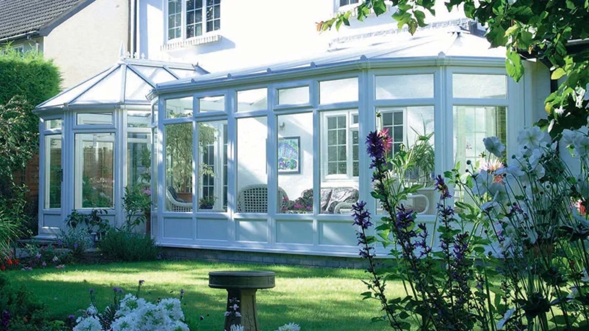 A large white P shaped conservatory behind a well-maintained lawn