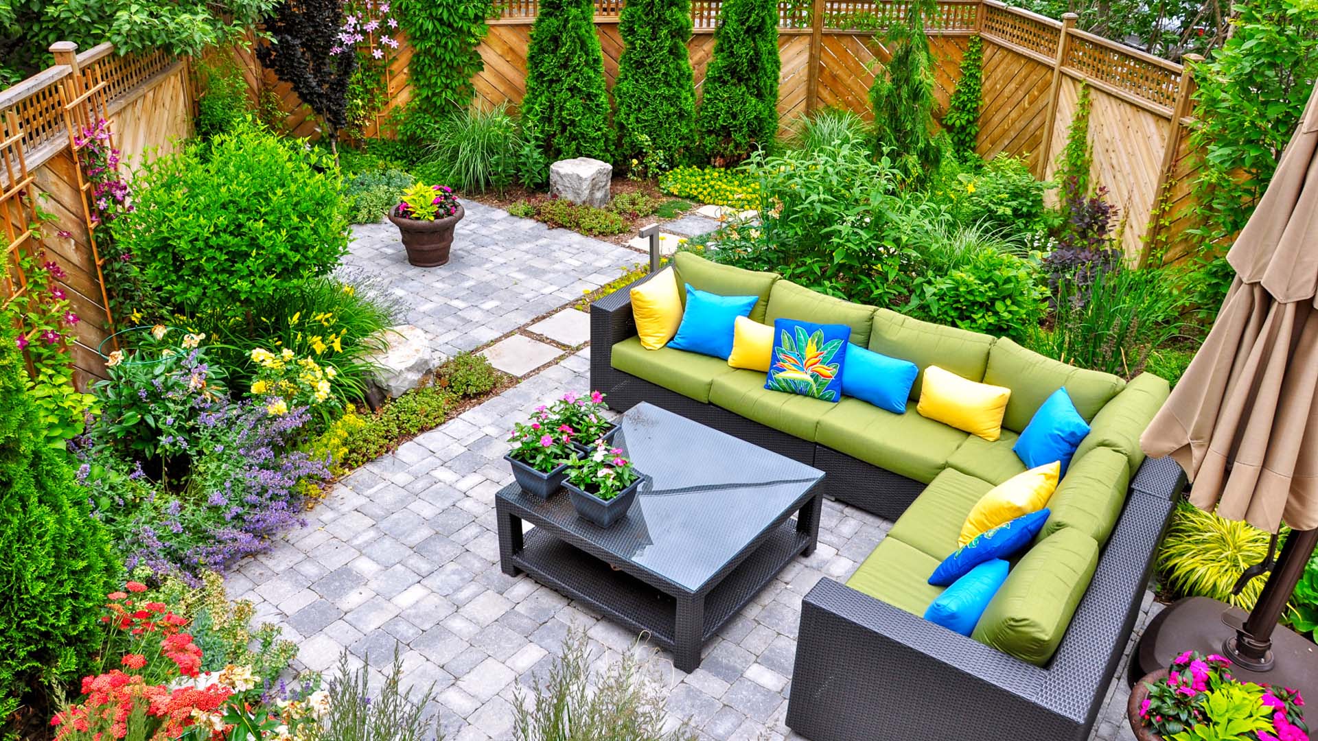 A beautiful small, urban backyard garden featuring a tumbled paver patio, flagstone stepping stones, and a variety of trees, shrubs and perennials add colour and year round interest