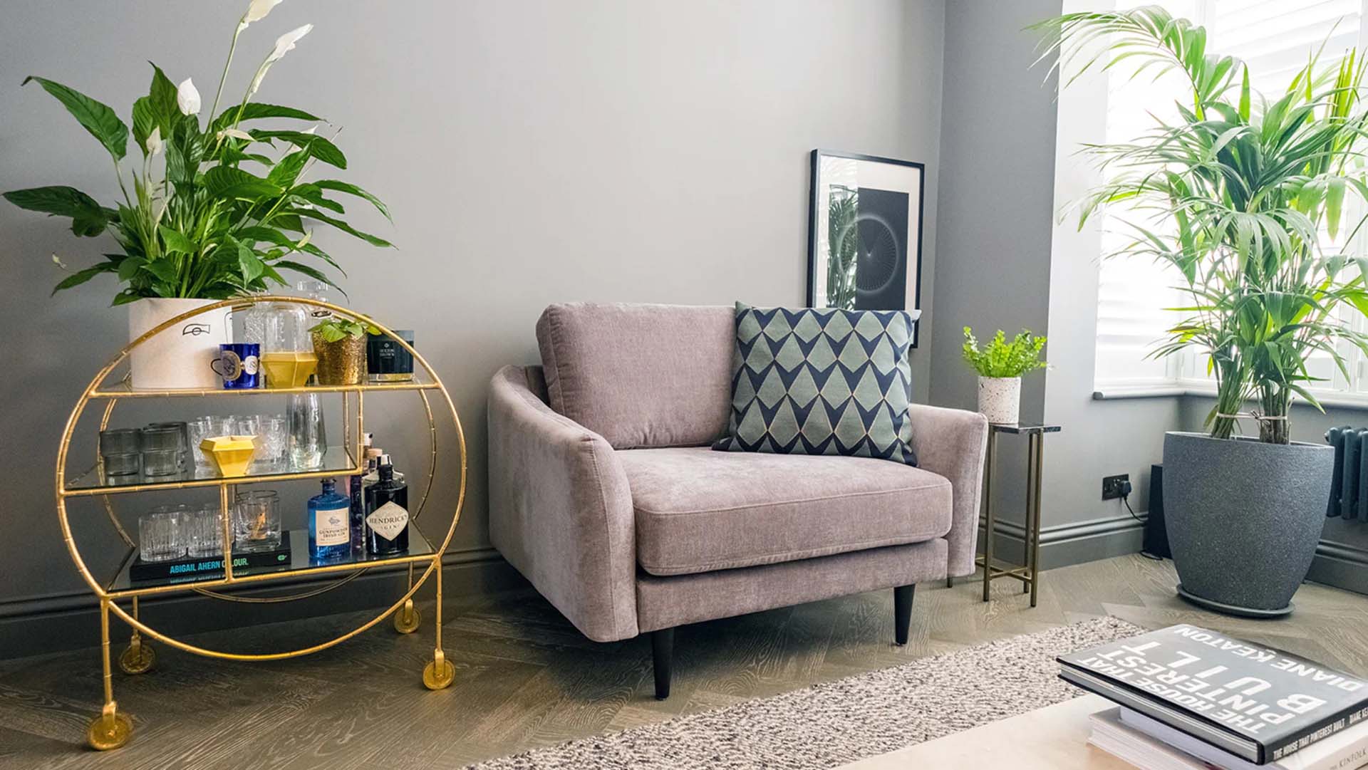 A small sofa next to a drinks trolley and large house plant.