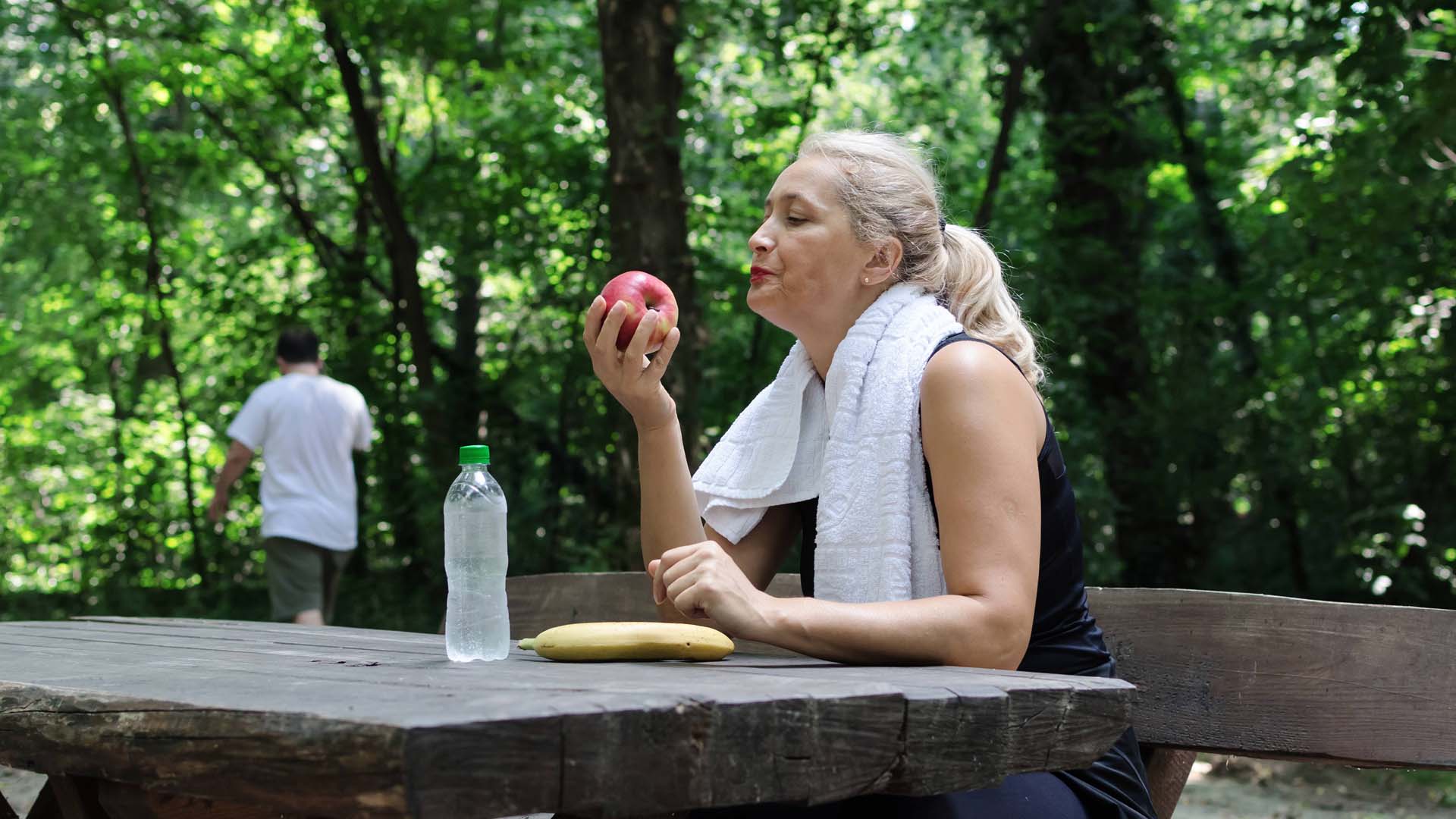 Adult woman sitting in park and eating apple.