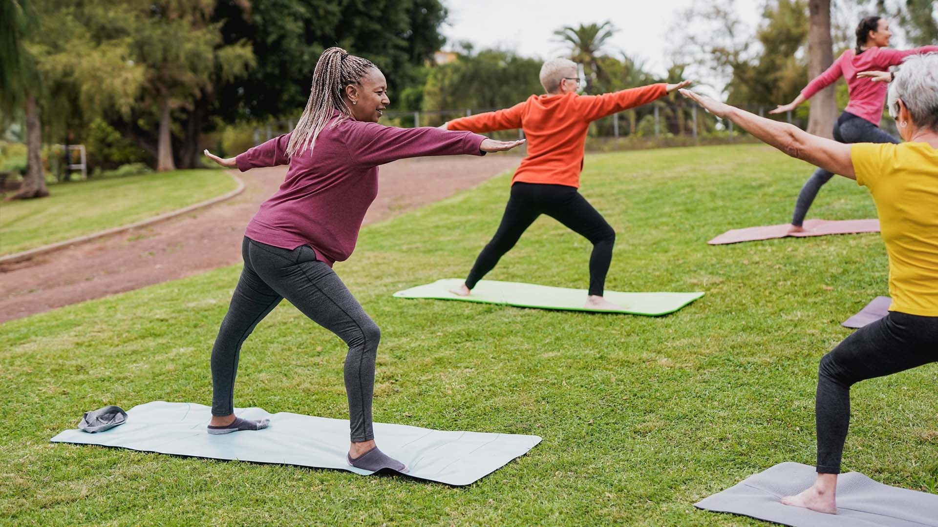A group of women practising the Warrior Two yoga position in an outdoor yoga class