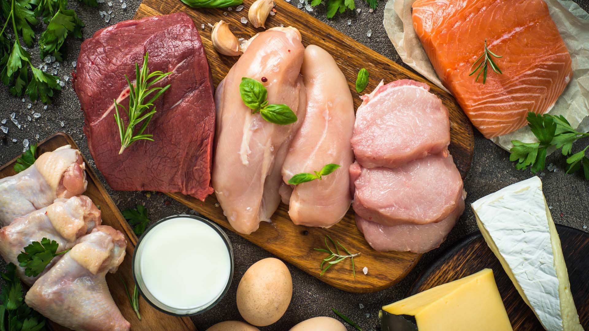 Raw meat on a chopping board surrounded by other protein like cheese and eggs