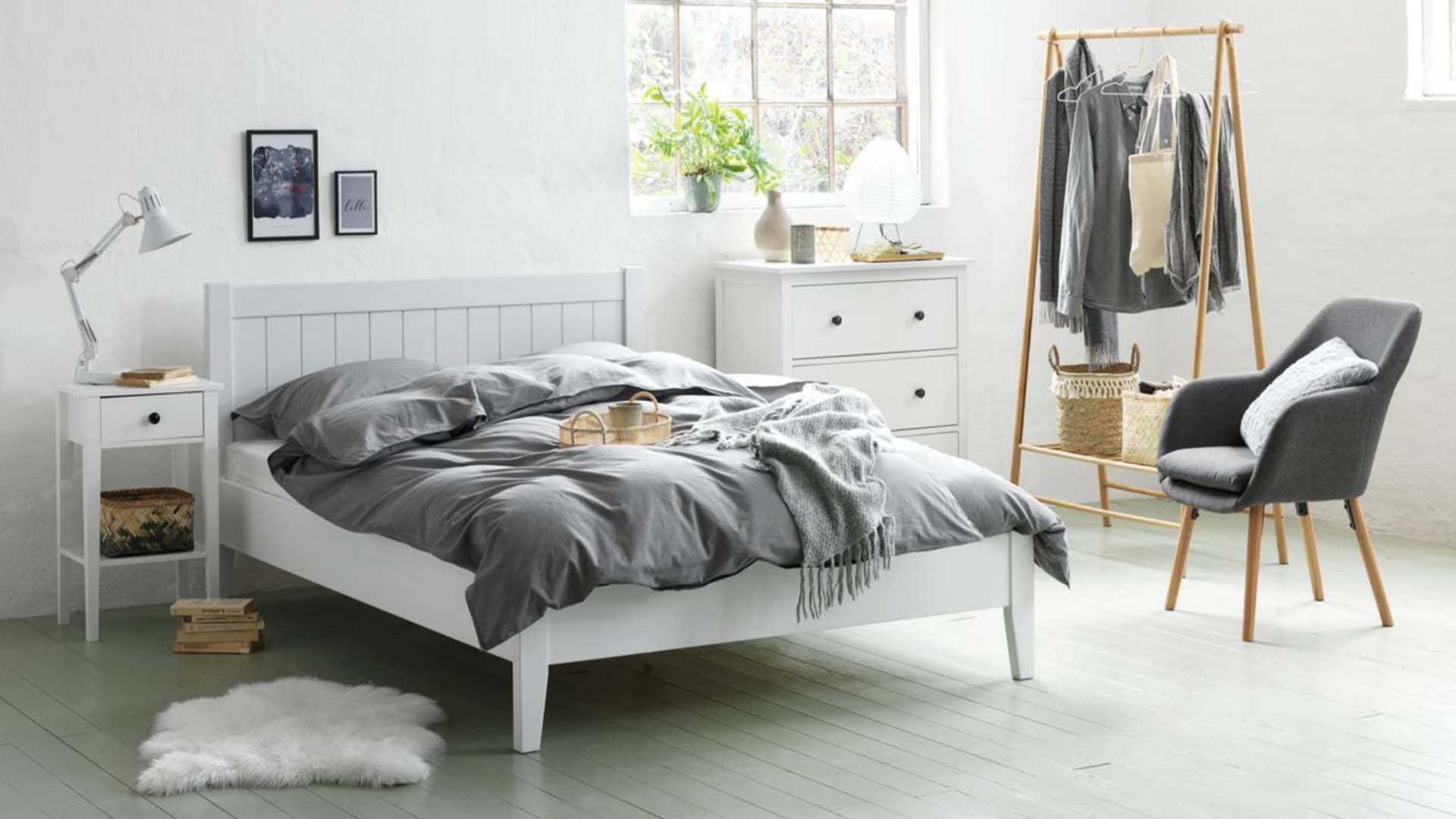 A bedroom with Scandi-style white bedside furniture and grey soft furnishings including bedding and an armchair