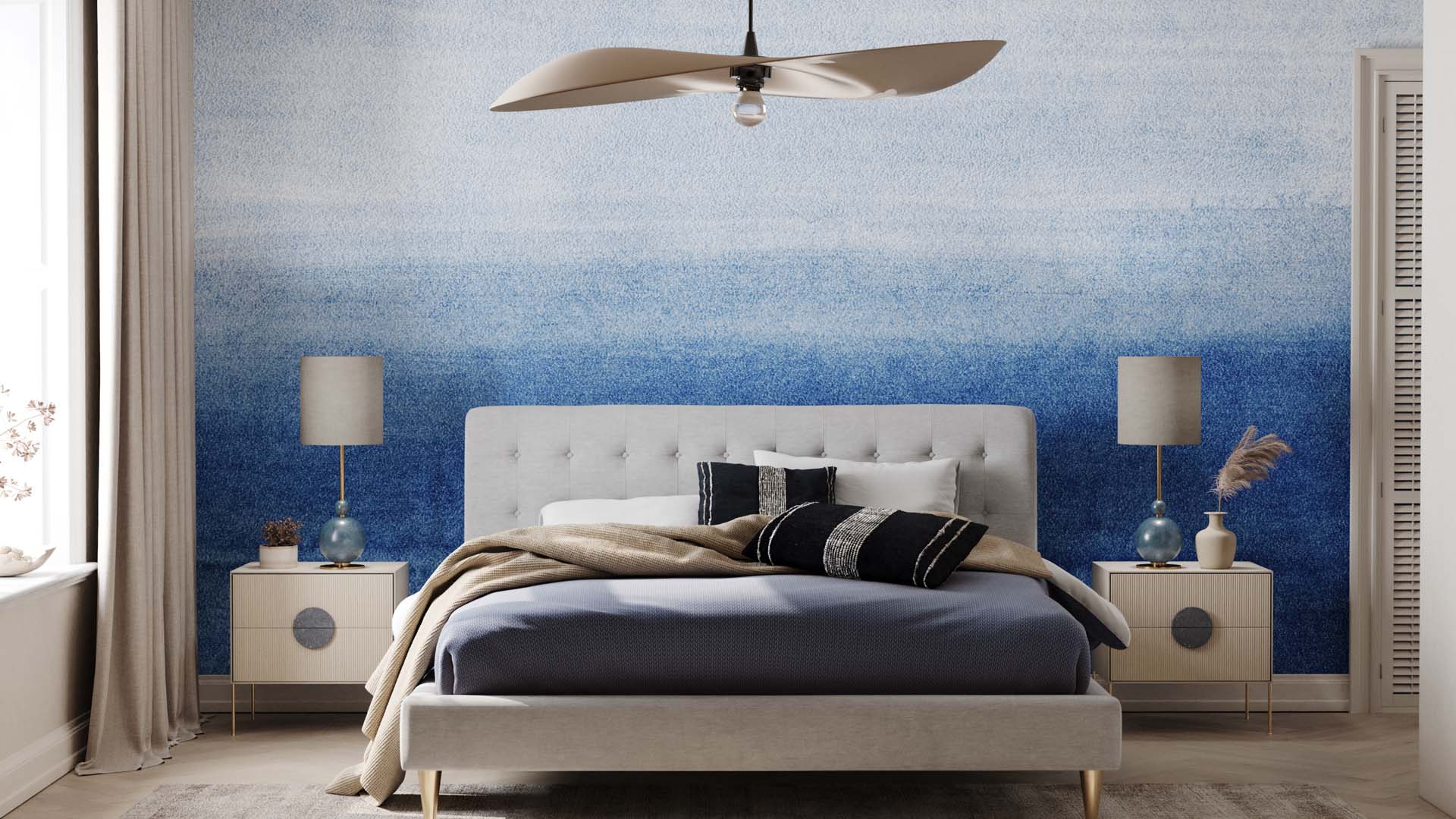 A bedroom with an ombre-effect wall in shades of blue and white, with a dhouble bed in shades of grey and bedside tables.